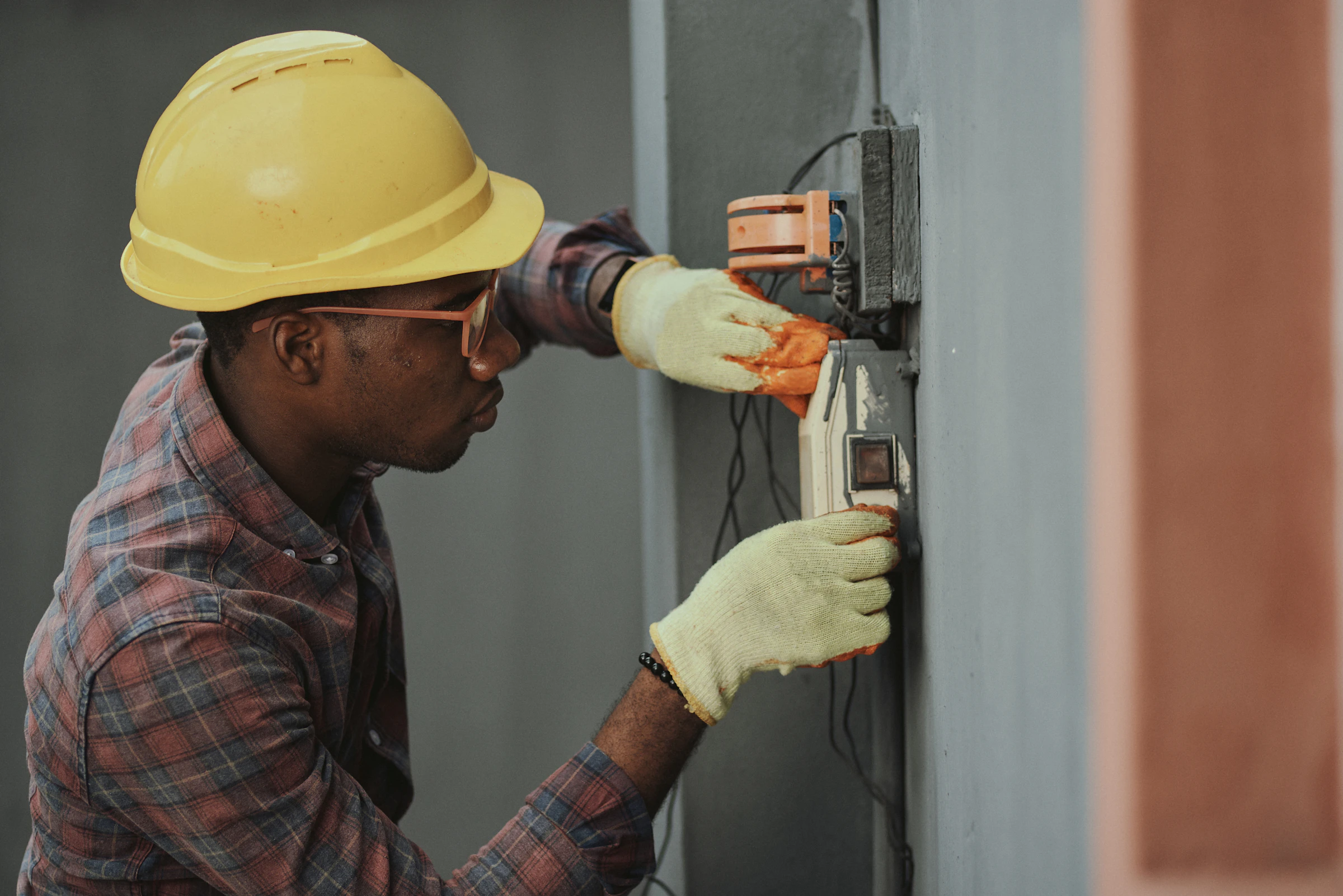 Electrician in a hard hat testing wiring at a wall panel