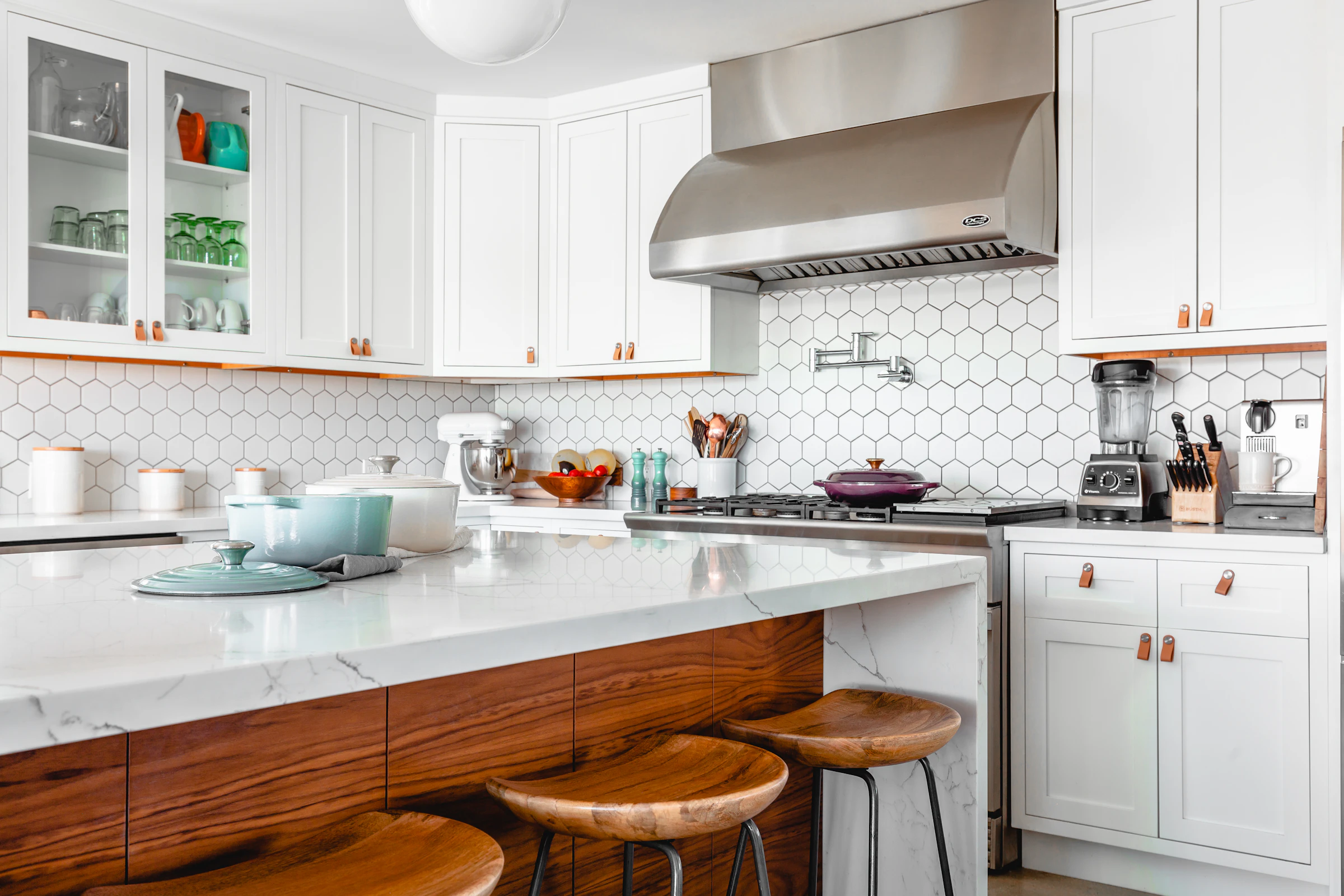 White kitchen with a marble island, timber bar stools and glass-front cabinets