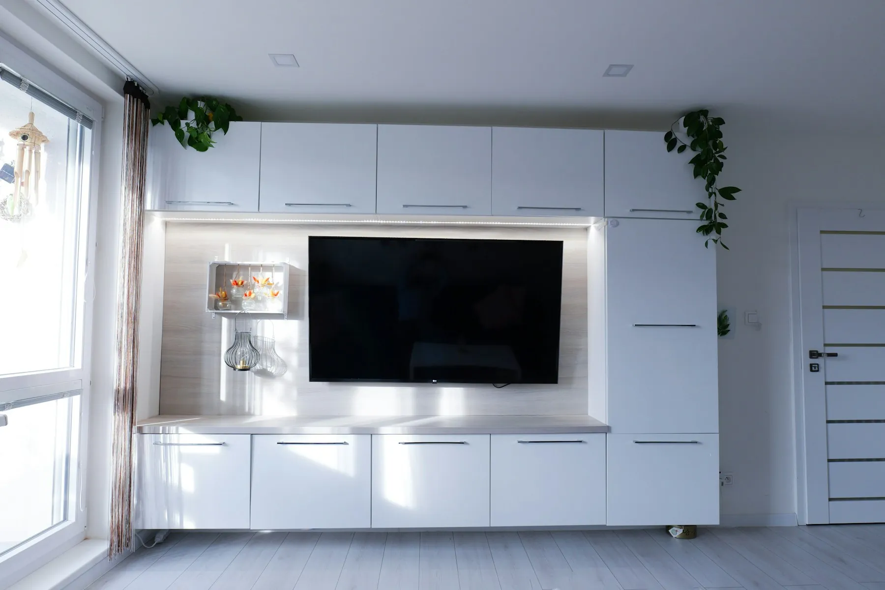 Wall-to-wall white TV unit with a backlit panel and storage above and below