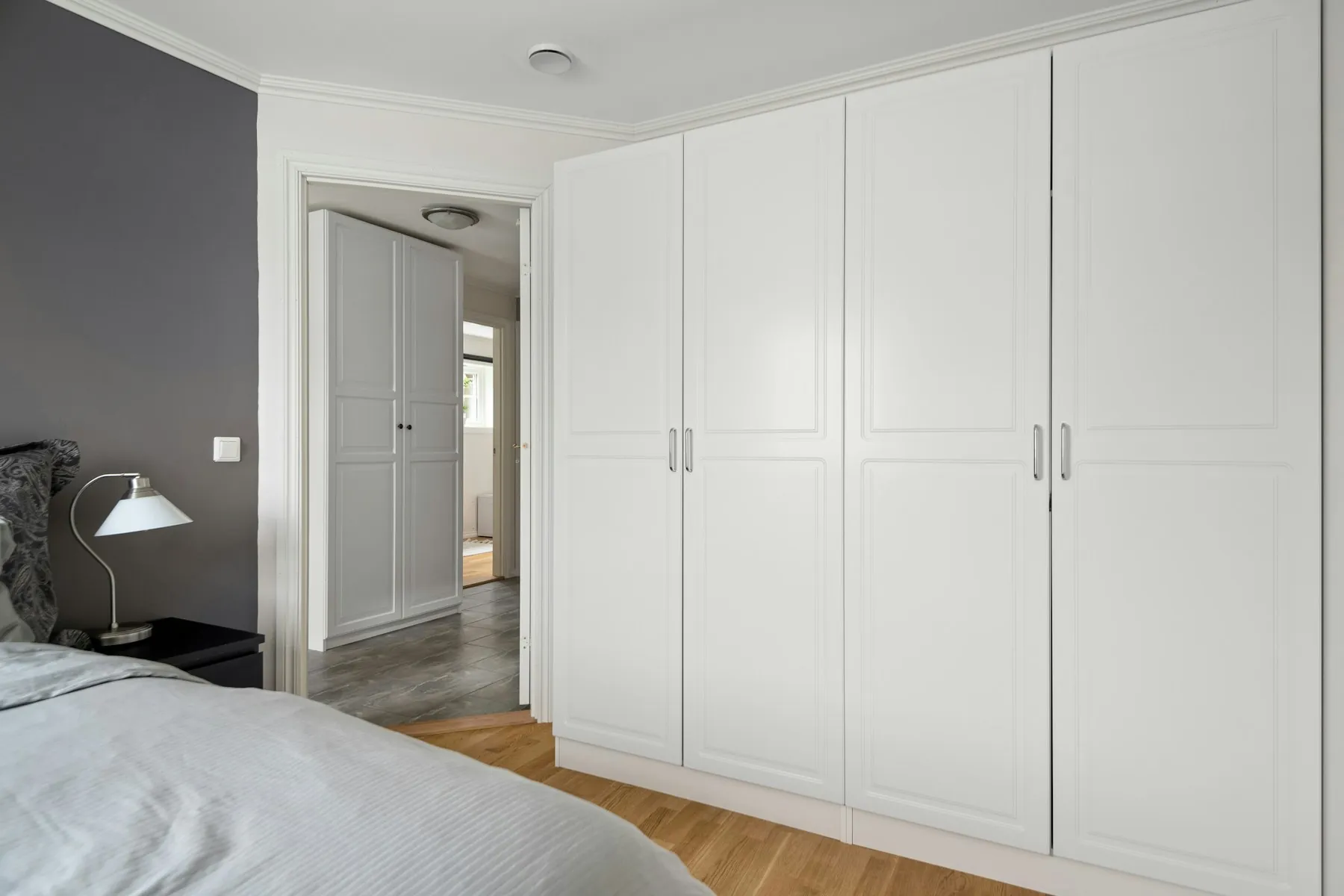 White hinged-door wardrobe with panelled shutters along a bedroom wall